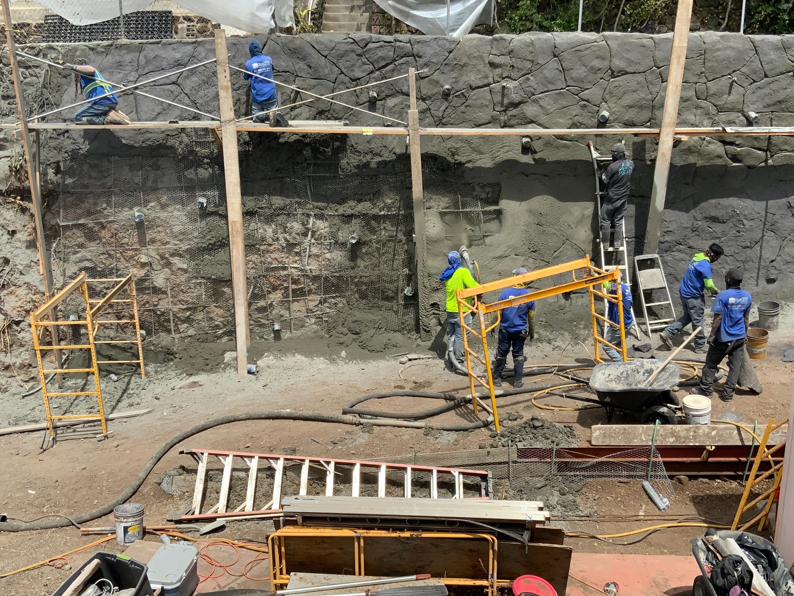 Crew on scaffolding building a hillside lava rock veneer wall