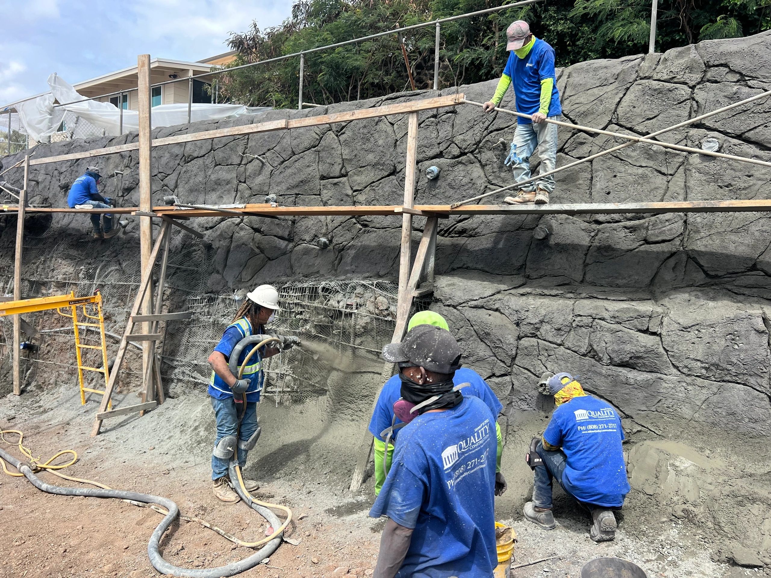 Crew sculpting a structural lava rock veneer on a retaining wall